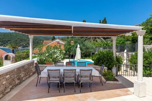 An outdoor patio with a covered table and chairs, a swimming pool, and a stone wall.
