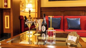 Un hall de hotel con un sofá rojo, una mesa de vidrio con copas de vino, una botella de vino, una vela y un certificado enmarcado.