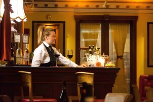Angolo bar con un barista, bancone e diverse bottiglie di alcolici.