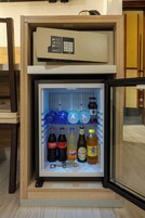 A minibar with a beverage dispenser and a small refrigerator containing various drinks and a bottle of water.