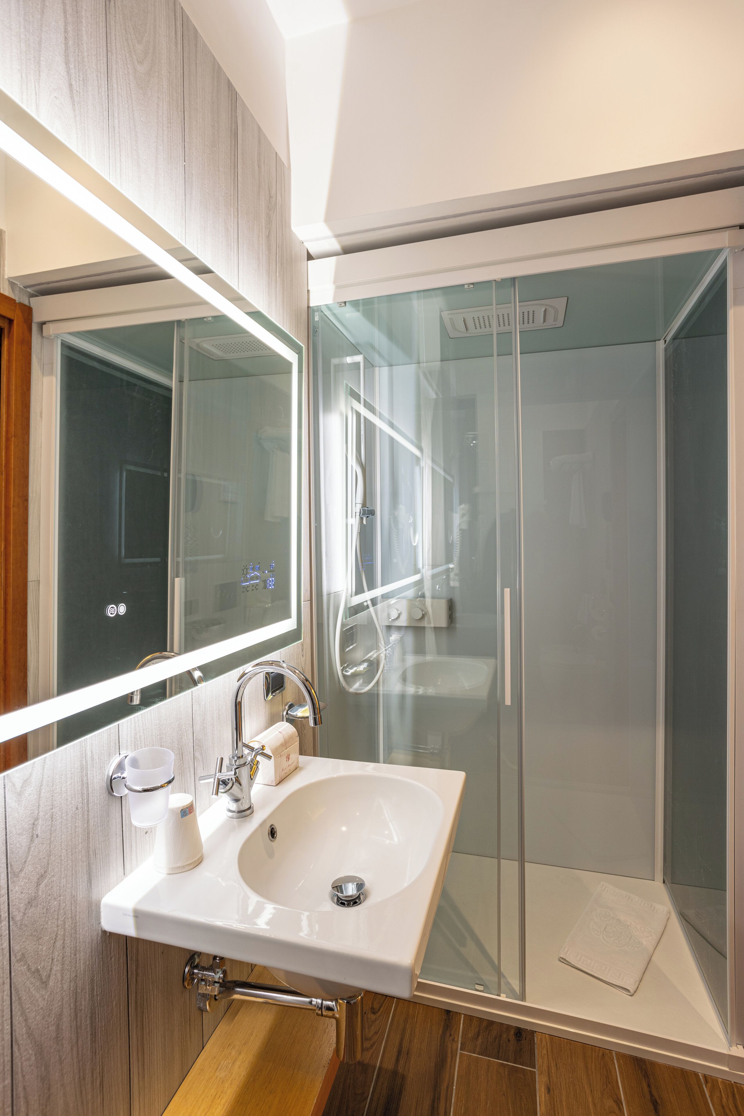 Une salle de bain moderne avec une douche à parois de verre, un lavabo blanc et un grand miroir.