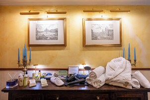 Una reception di hotel con fotografie in bianco e nero di una veduta cittadina incorniciate, un candelabro, articoli da toilette, un accappatoio e un asciugacapelli.