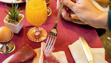 Un piatto per la colazione con uova, pancetta e formaggio, un bicchiere di succo d'arancia e una forchetta e un coltello su una tovaglia rossa.