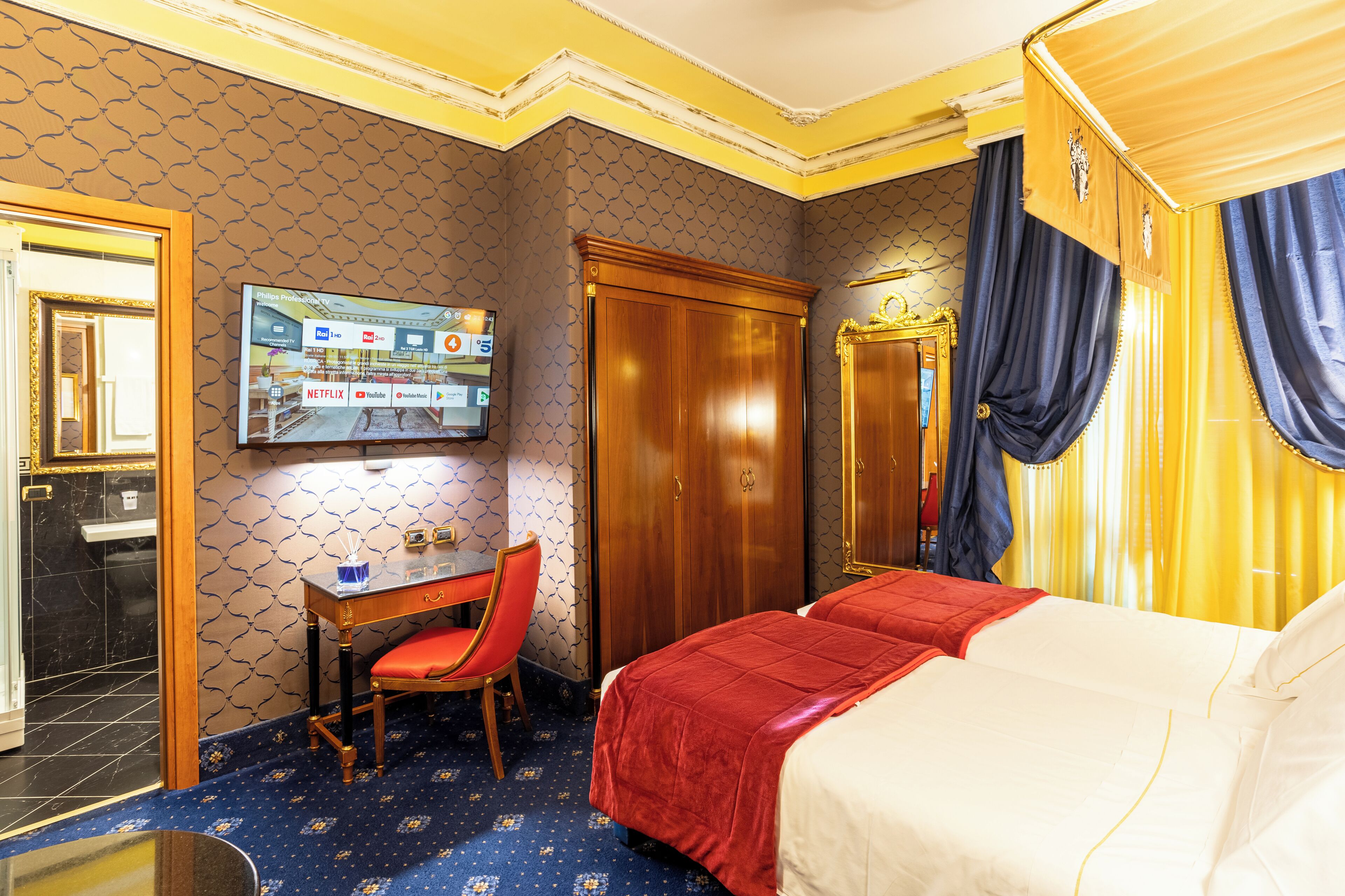 A hotel room with a bed, a desk, a chair, a television, and a wardrobe.