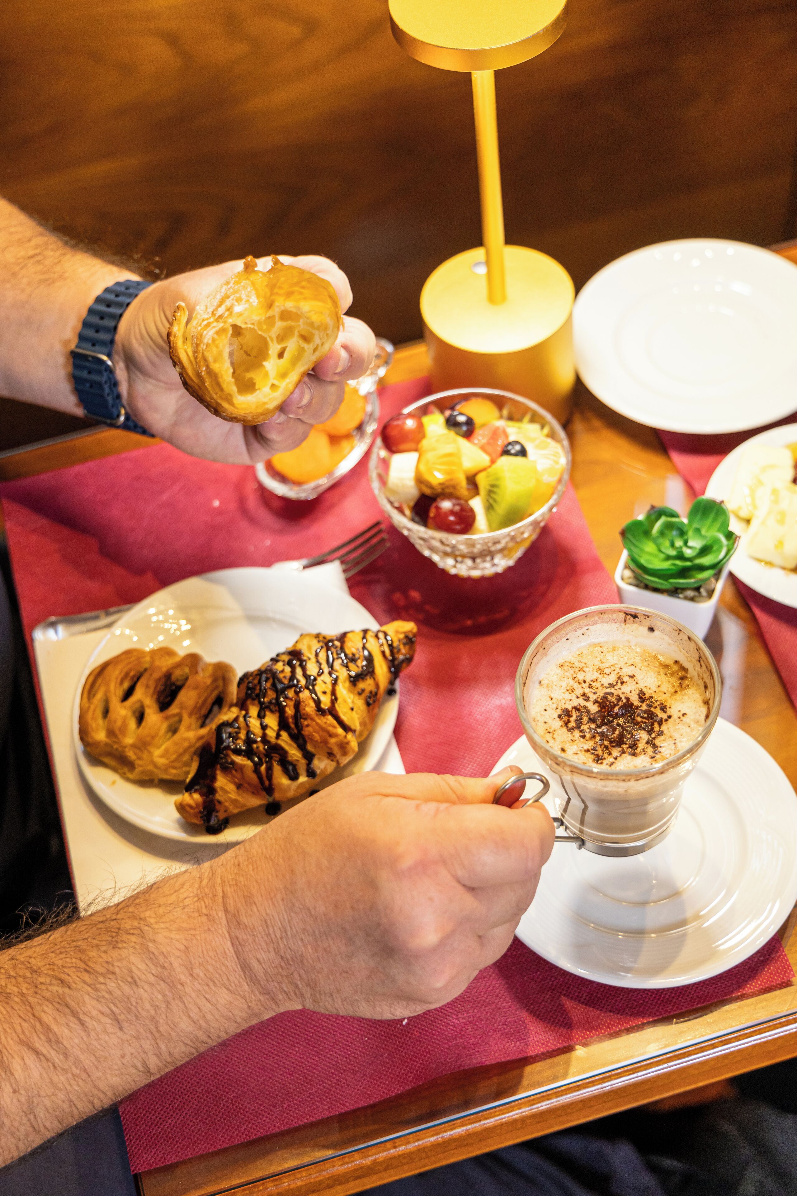 A breakfast tray with a croissant, fruit salad, and a cup of coffee.