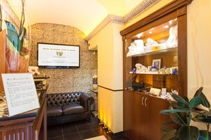 Egy fekete bőrkanapéval, recepcióval, keretezett táblával és egy növénylyel berendezett szállodai előtér.