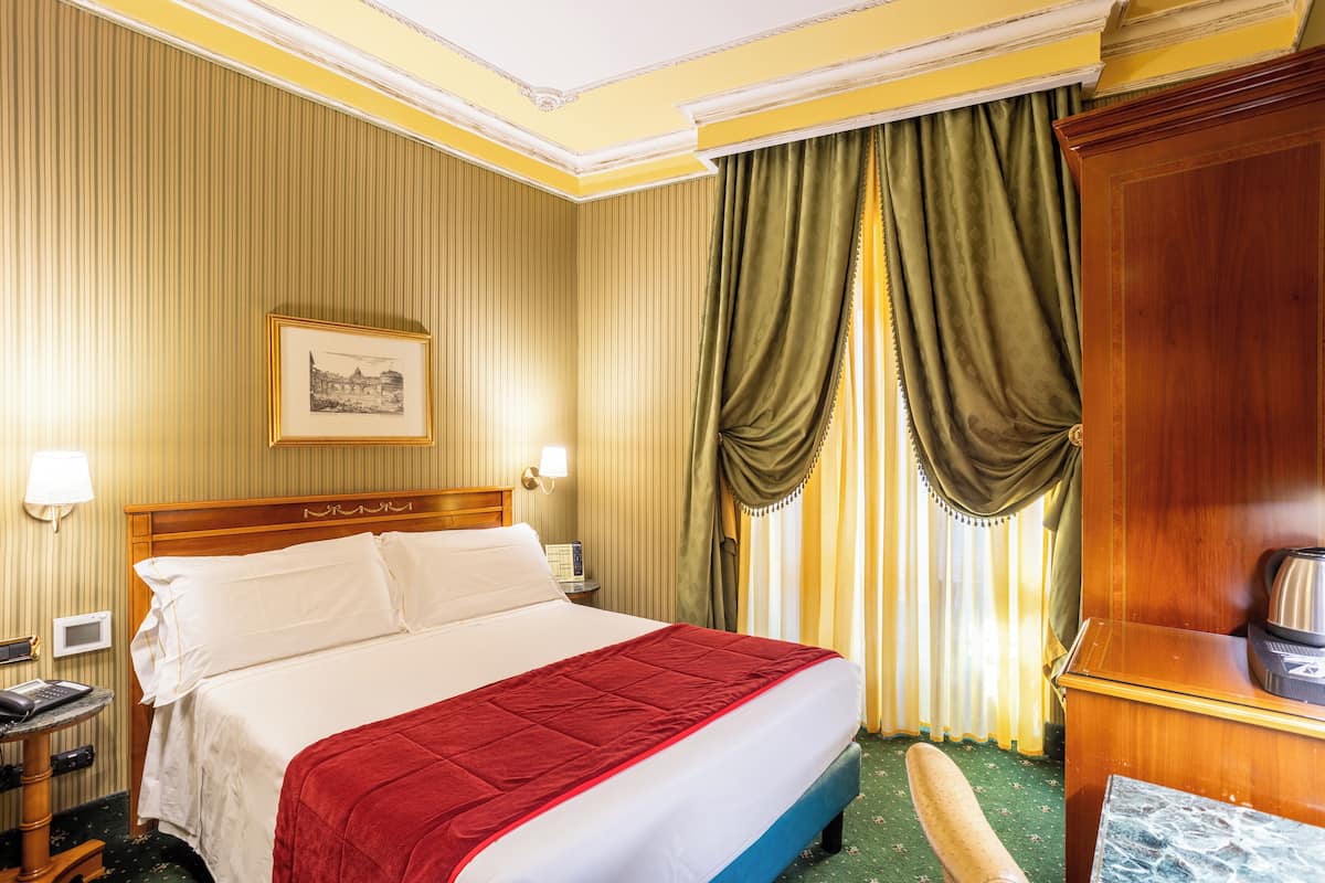 A hotel room with a large bed, a wooden headboard, a bedside table with a lamp, a telephone, and a picture on the wall.