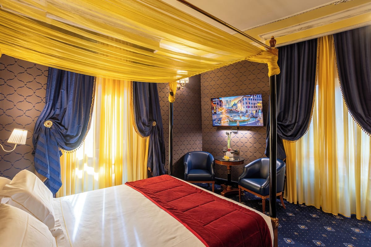 A hotel room with a large bed, a desk with two chairs, a television, and curtains.