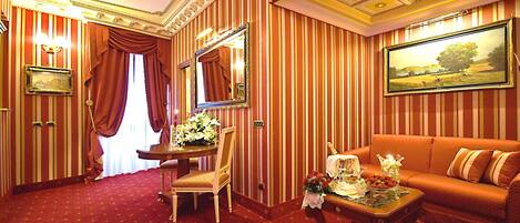A room with striped wallpaper, a sofa, a chair, a table with a vase of flowers, and a framed picture on the wall.