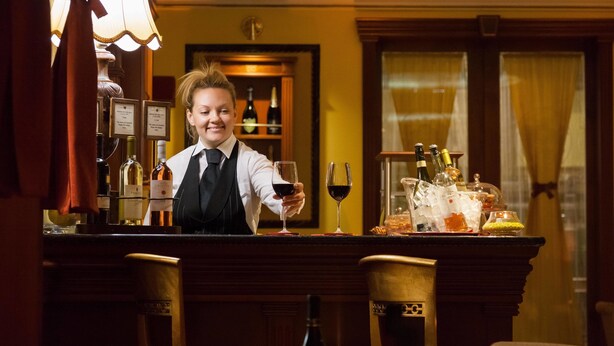 Zona de bar con un barman, una copa de vino y una botella sobre la barra.