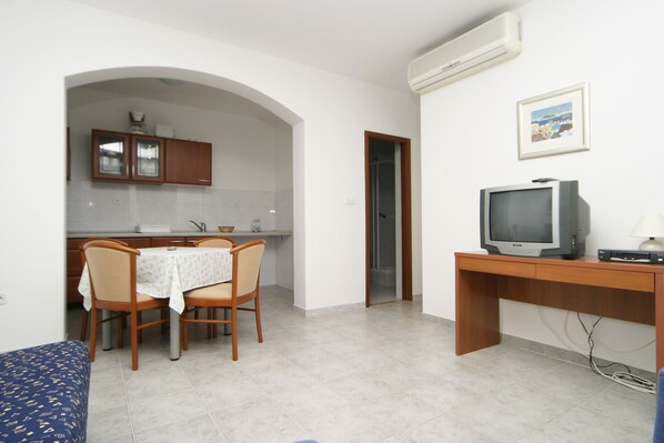A compact living space with a dining area, a TV on a wooden stand, and a small kitchenette.