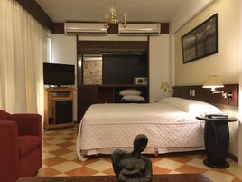 Una habitación de hotel con una cama, televisor, escritorio, lámpara y una estatua.