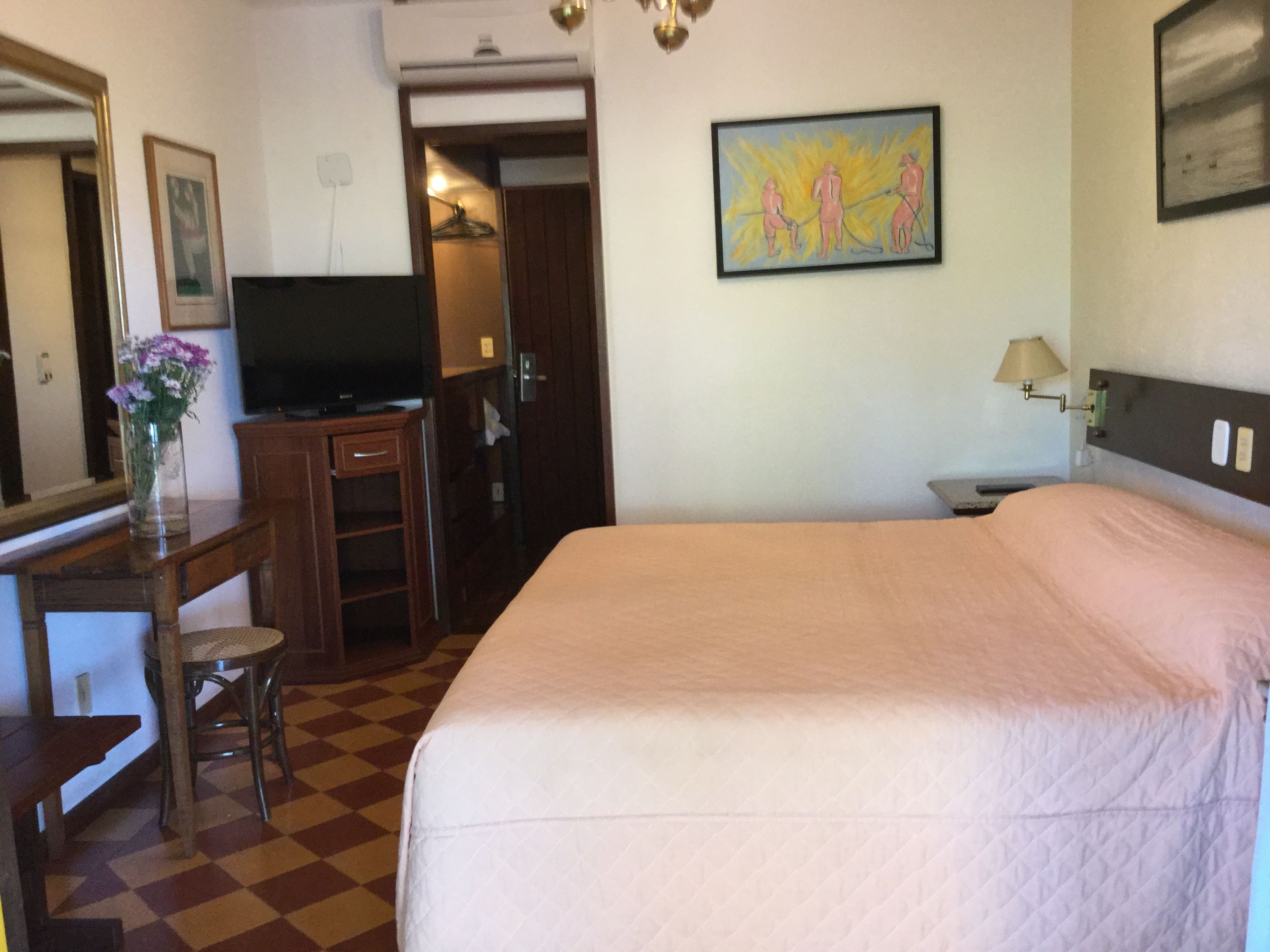 Habitación de hotel con cama, escritorio con silla, televisión, un cuadro en la pared y una lámpara.