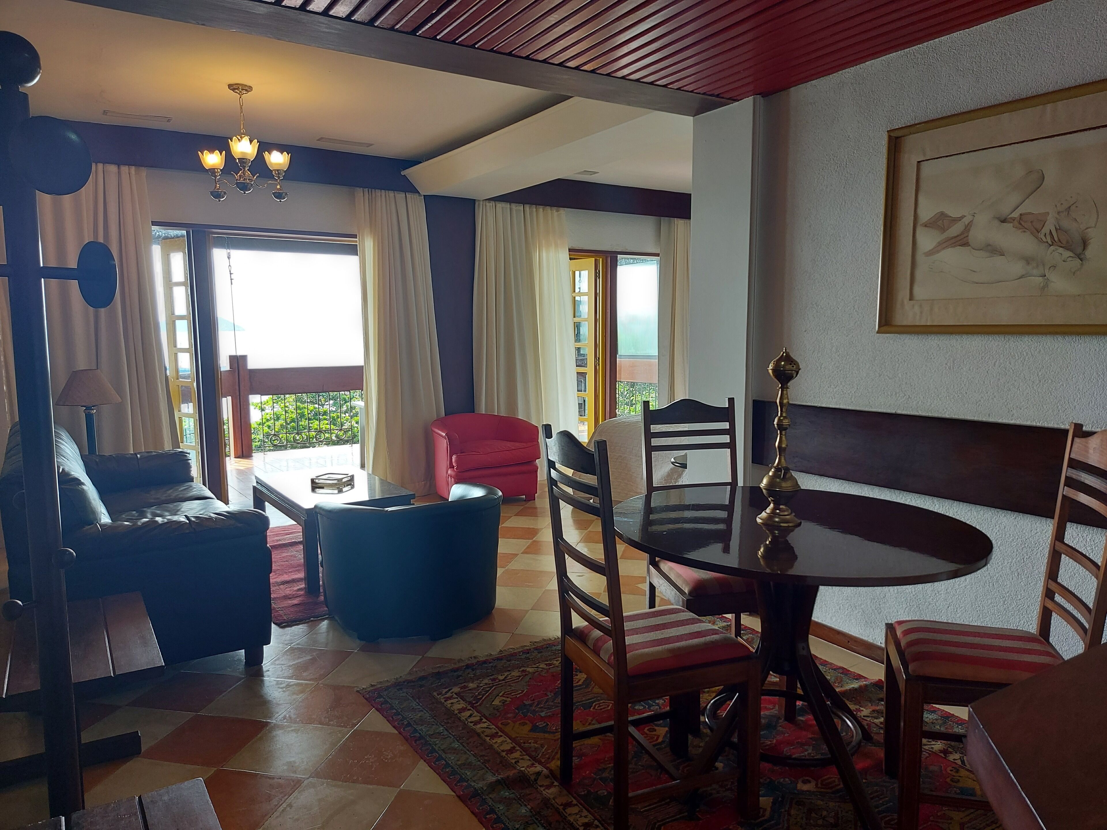 A room with a dining table, chairs, a sofa, a red armchair, and a chandelier.