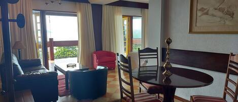 A room with a dining table, chairs, a sofa, a red armchair, and a chandelier.