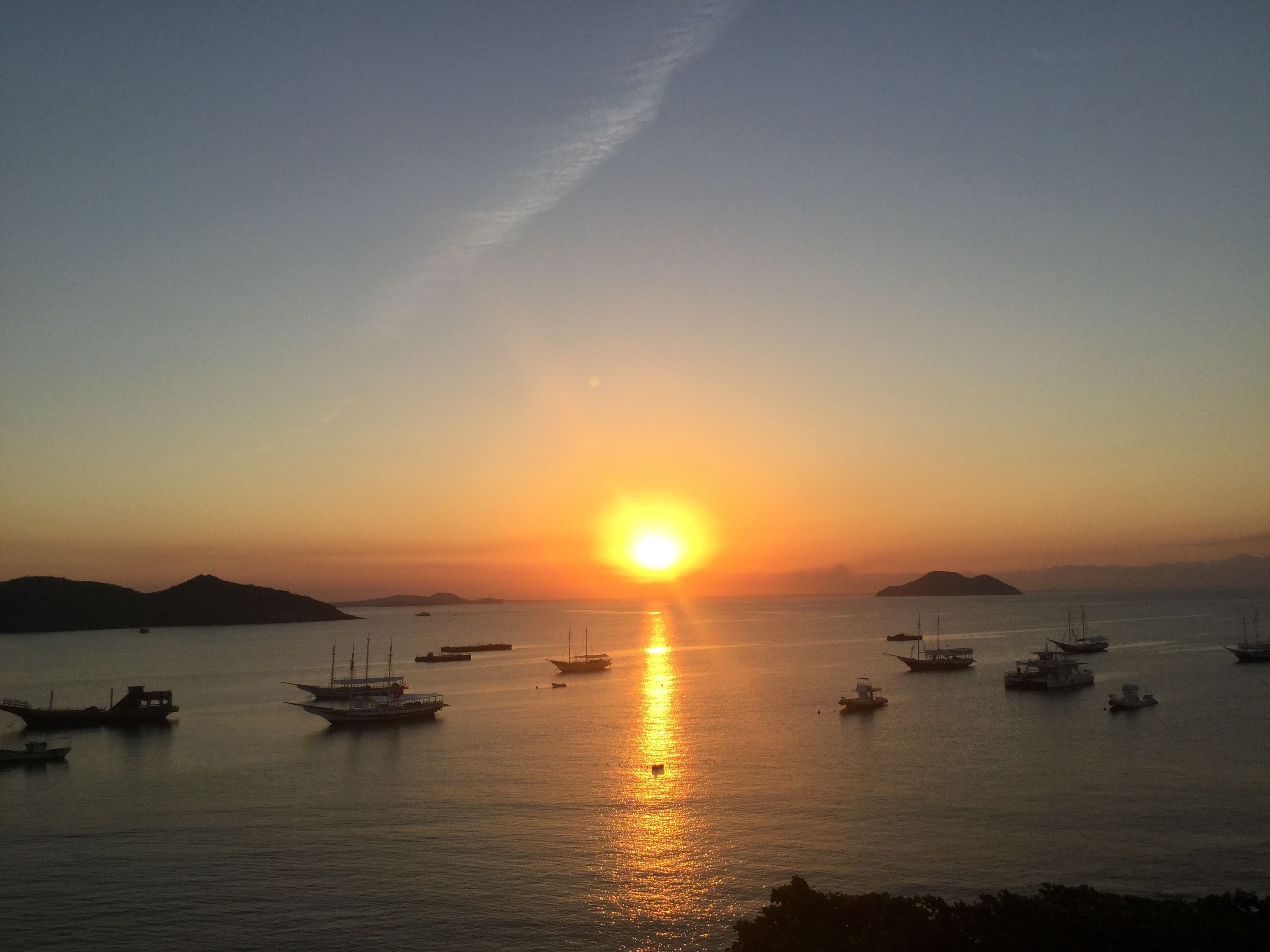 Um pôr do sol sobre um mar calmo com vários barcos.
