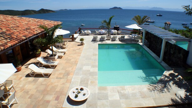 Un espace piscine avec des chaises longues et des parasols, une piscine et une vue sur la mer.
