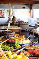 A dining area with a variety of food items, including a chocolate cake, fruits, and a plate of pastries.