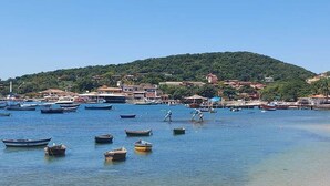 Une zone côtière où des bateaux sont amarrés près du rivage, avec une plage et des bâtiments situés sur une colline en arrière-plan.