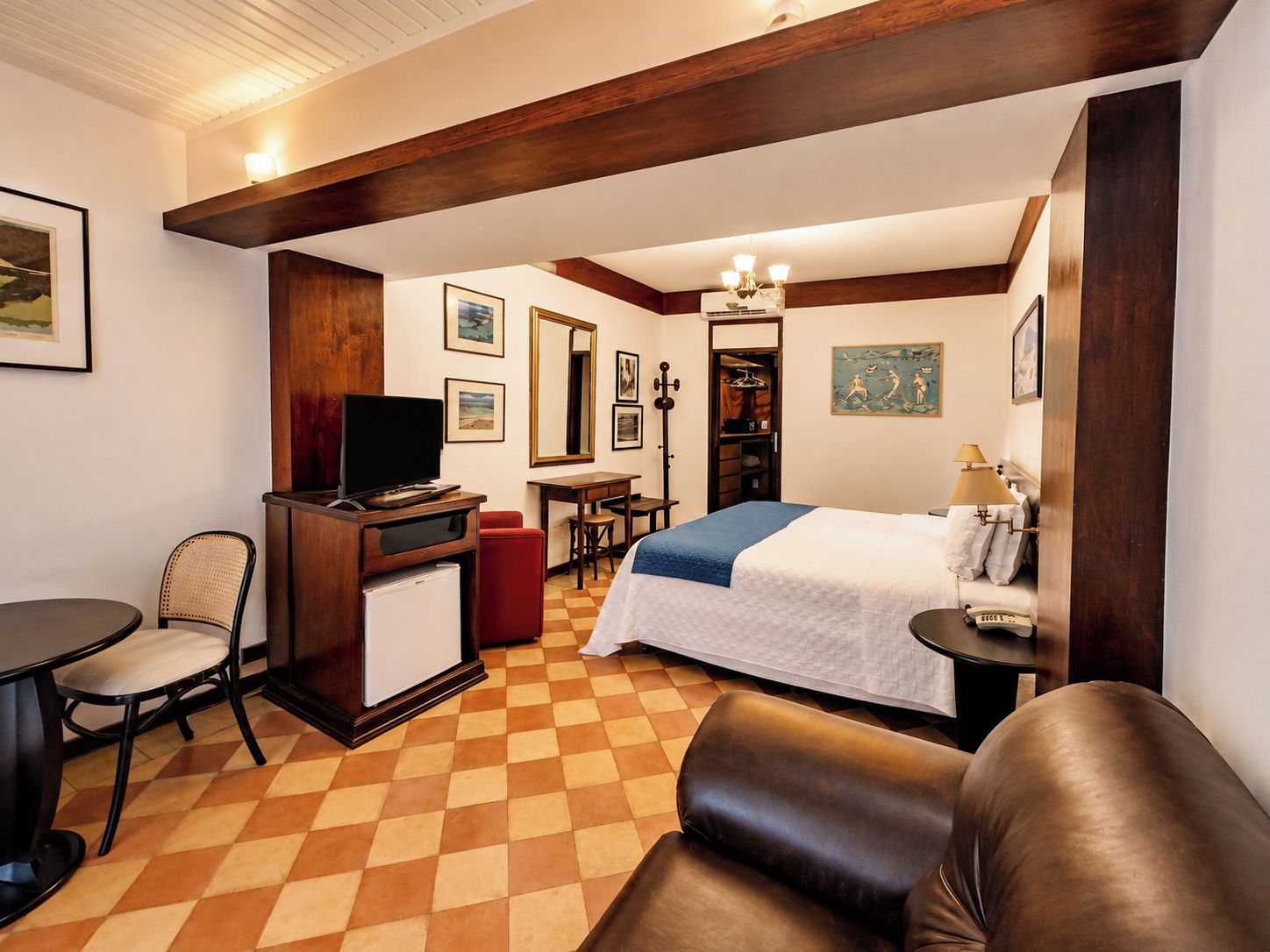Een hotelkamer met een bed, bureau, stoel, televisie en kunst aan de muren.
