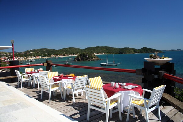 A deck with white chairs and tables, overlooking a coastal area with boats and hills. - Sailing Hotel & Spa (Búzios)