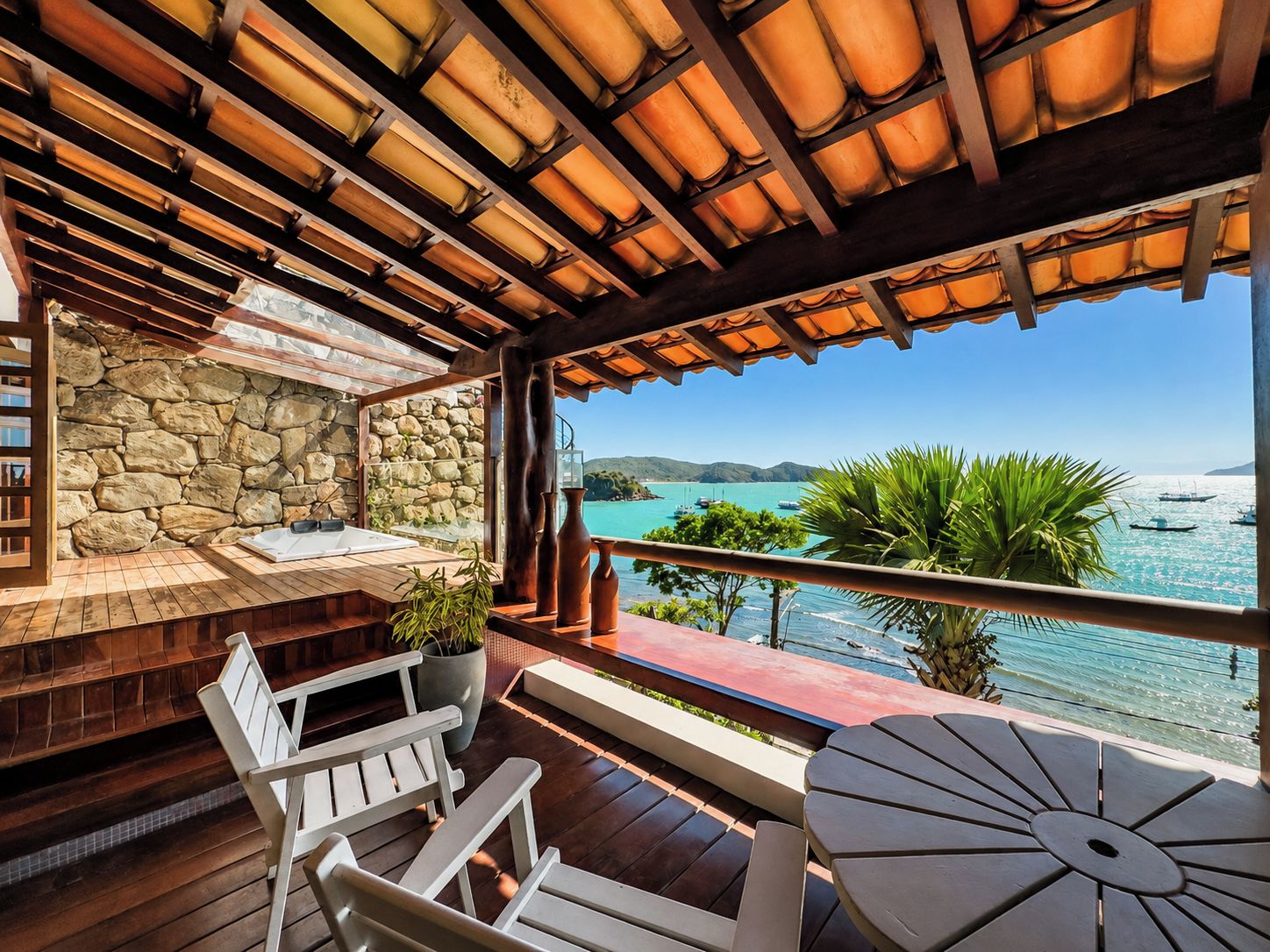 Une terrasse en bois avec un mur en pierre, des sièges d’extérieur et une vue sur la mer.