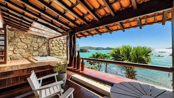 Una terraza de madera con un muro de piedra, mobiliario exterior y vista al mar.