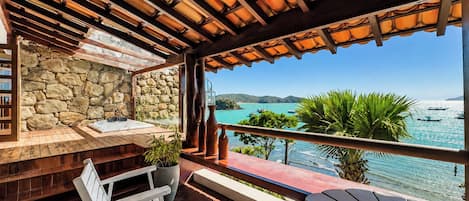A wooden deck with a stone wall, outdoor seating, and a view of the sea.
