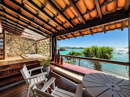 Una terraza de madera con un muro de piedra, mobiliario exterior y vista al mar.