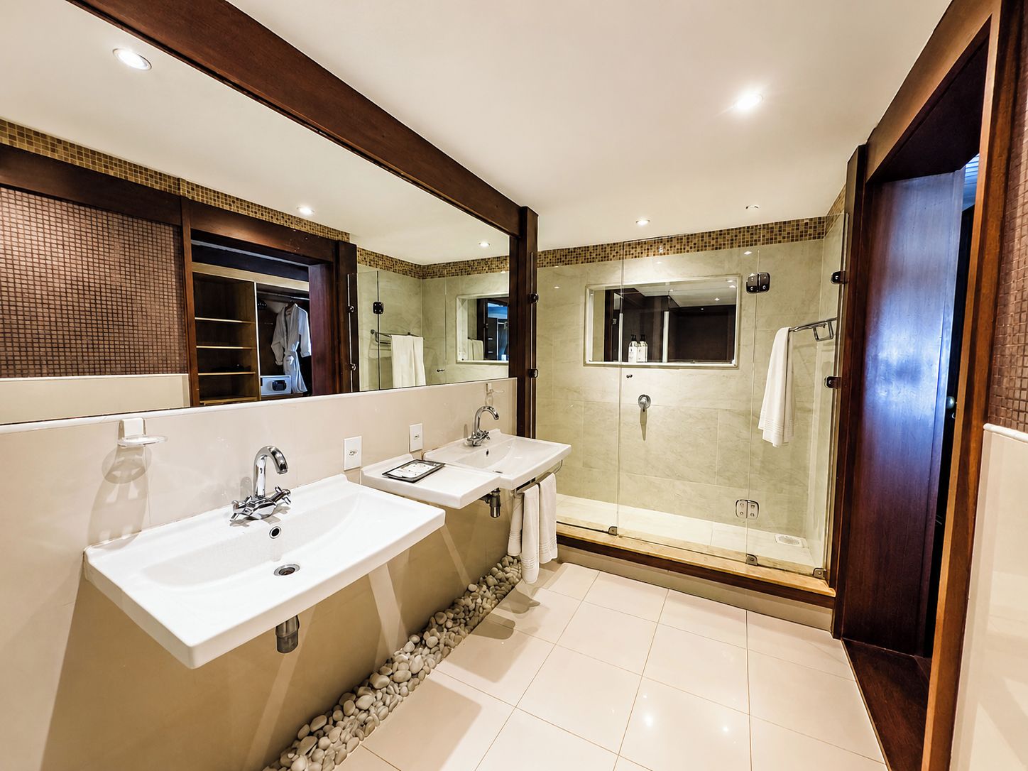 A modern bathroom with two sinks, a glass-enclosed shower, and a large mirror.