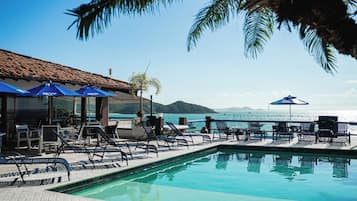 Un área junto a la piscina con sillones y sombrillas, con vistas a un cuerpo de agua y un paisaje montañoso.