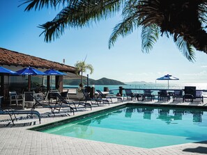 A poolside area with lounge chairs and umbrellas, overlooking a body of water and a mountainous landscape. - Sailing Hotel & Spa (Búzios)