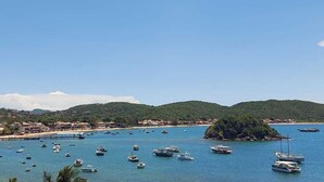 Un paysage côtier avec des bateaux sur l’eau, une petite île et une ville en arrière-plan.