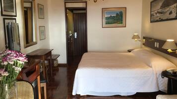 Quarto de hotel com uma cama grande, uma escrivaninha com cadeira, um vaso de flores e quadros nas paredes.