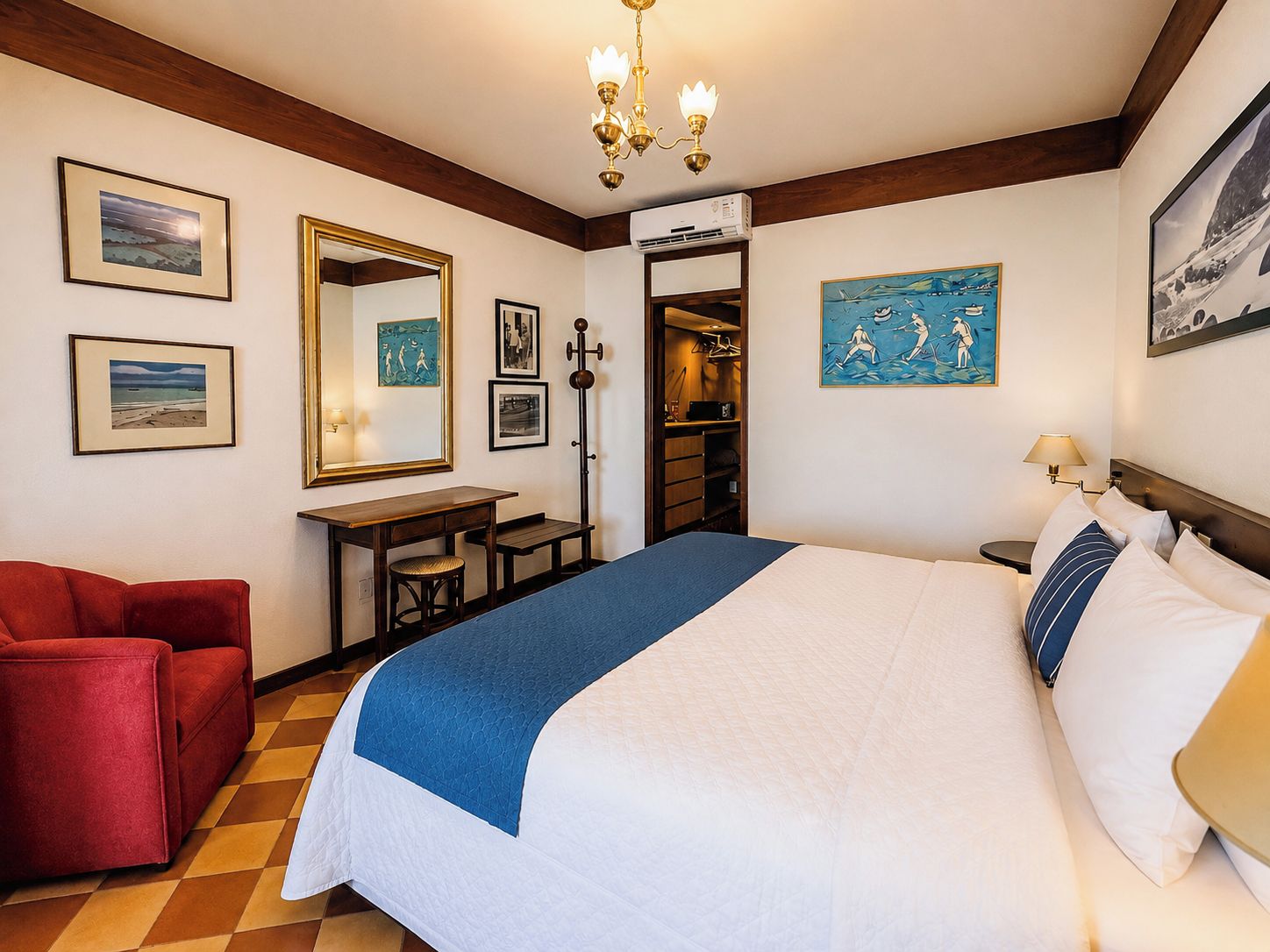 Habitación de hotel con cama, escritorio, silla, espejo y obras de arte en las paredes.