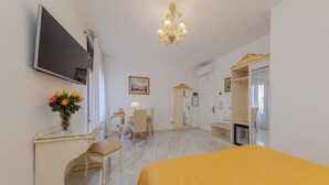 Ein Hotelzimmer mit Bett, Schreibtisch, Stuhl, Fernseher, einer Chandelierleuchtre und einem Spiegel.
