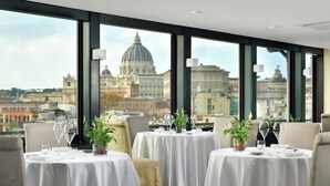 A restaurant with tables set for dining, large windows offering a city view, and a green carpeted floor. - Lemon Garden (Rome)