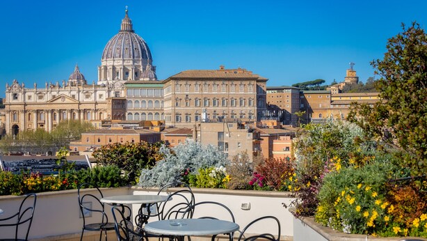 A view of a historic building with a large dome and classical architecture, overlooking a terrace with outdoor seating and lush greenery. - Lemon Garden (Rome)