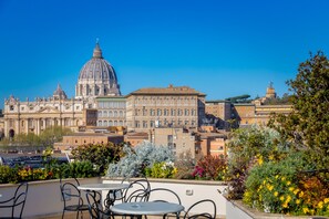 Vista de un edificio histórico con una gran cúpula y arquitectura clásica, que se alza sobre una terraza con asientos al aire libre y abundante vegetación.