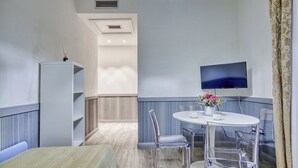A hotel room with a bed, a white table with chairs, a TV mounted on the wall, and a window with curtains. - Lemon Garden (Rome)