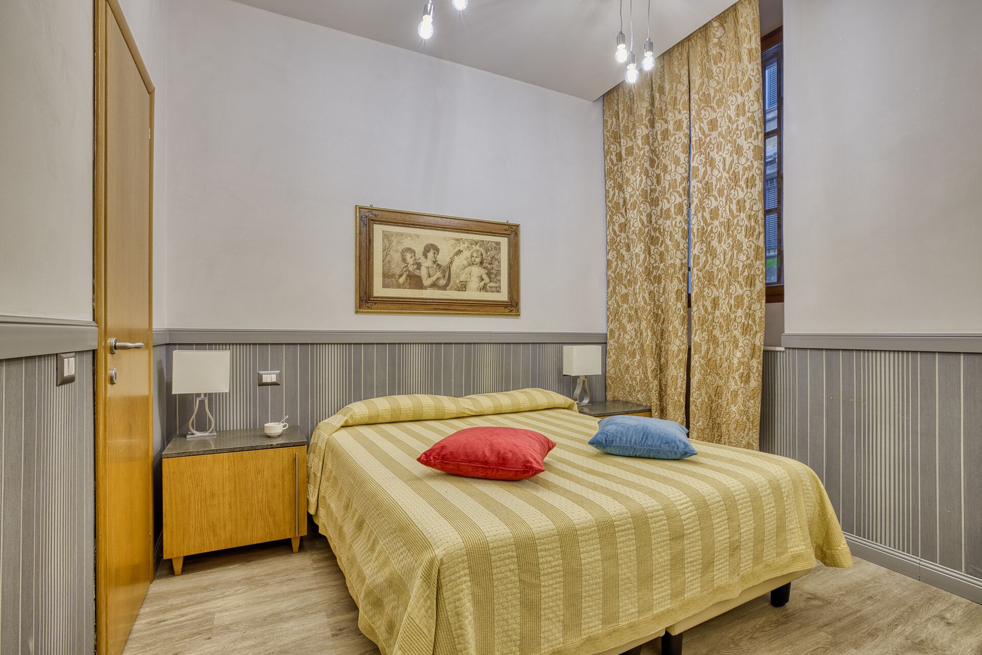 Ein Schlafzimmer mit einem Bett, Nachttischen, einem Fenster mit Vorhängen und einem gerahmten Bild.