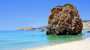 A clear blue sea with a rocky outcrop in the foreground and a sandy beach.