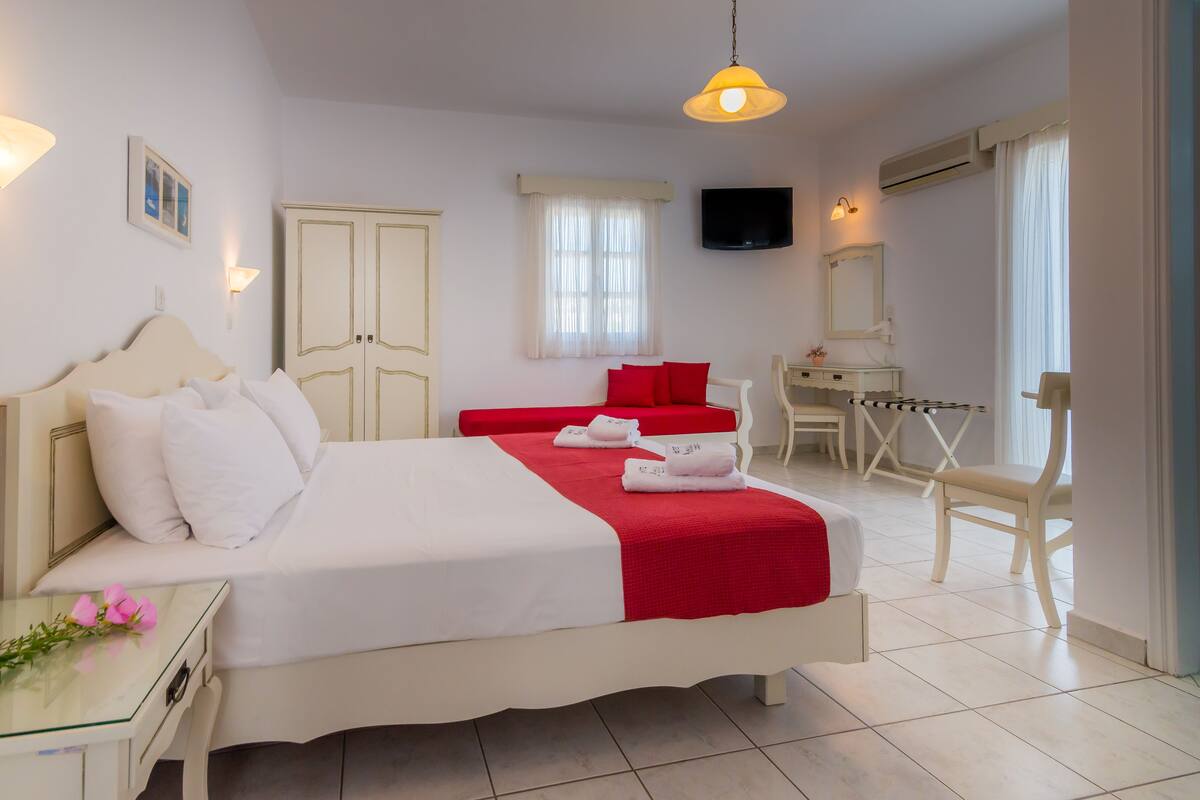 A hotel room with a bed, a desk, a chair, a TV, and a window with curtains.