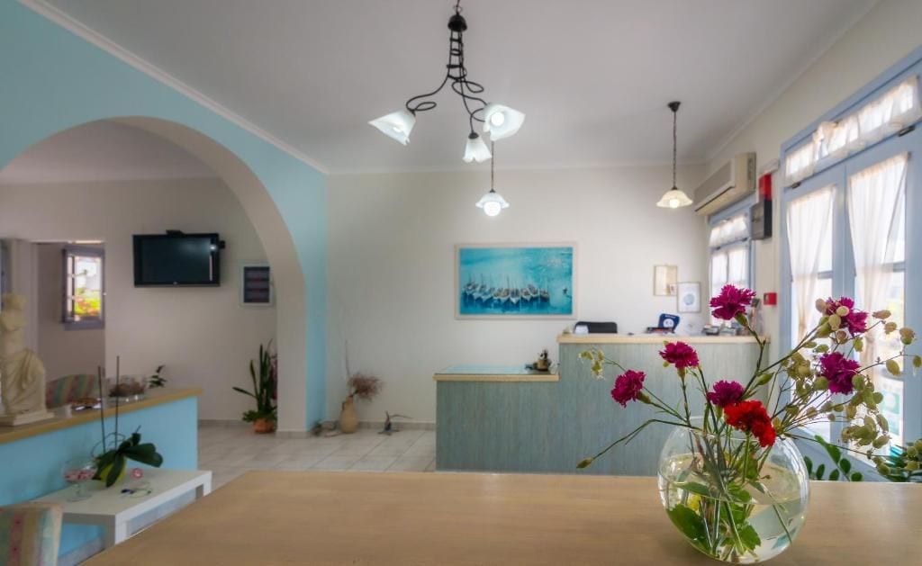 Un espace d’accueil avec un bureau, un tableau accroché au mur et un vase de fleurs posé sur la table.