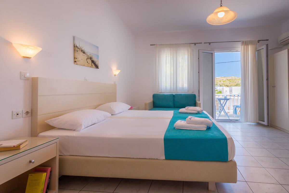 A hotel room with two beds, a balcony with a view, and a painting on the wall.