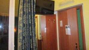 A room with a television mounted on the wall, a door with a green panel, and a window with curtains. - B & B Evergreen (Rome)