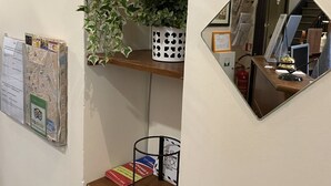 A room with a wooden shelf holding books and a potted plant, a bulletin board with maps, and a mirror reflecting a desk area. - B & B Evergreen (Rome)