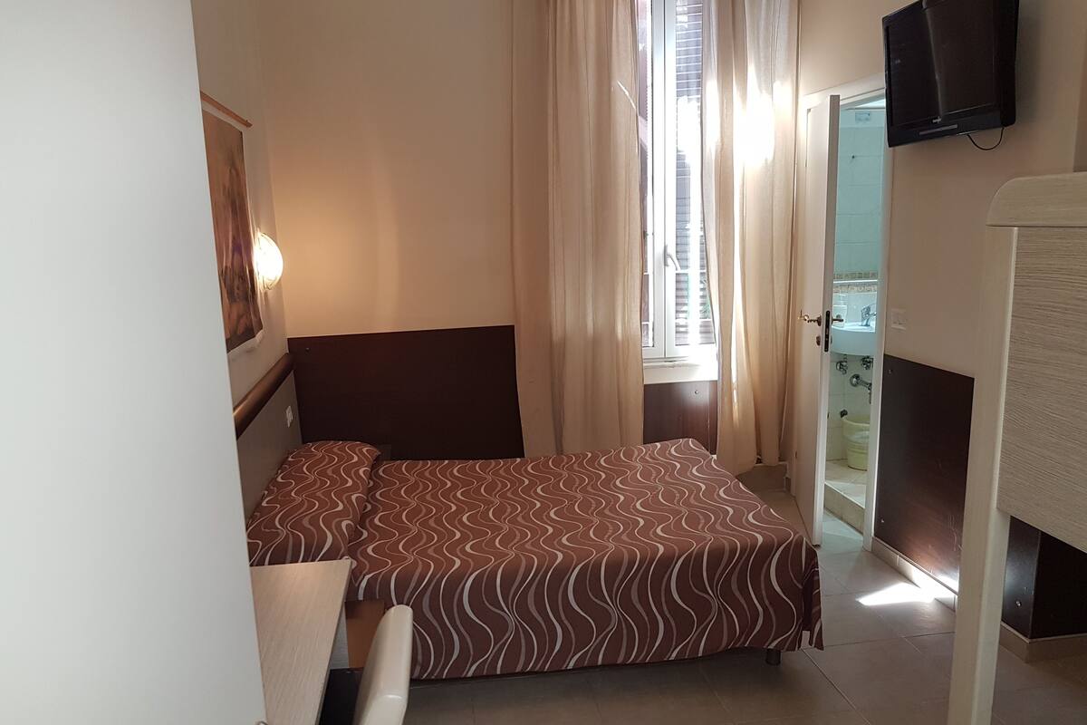 A hotel room with a bed, a television mounted on the wall, and a bathroom visible through an open door.