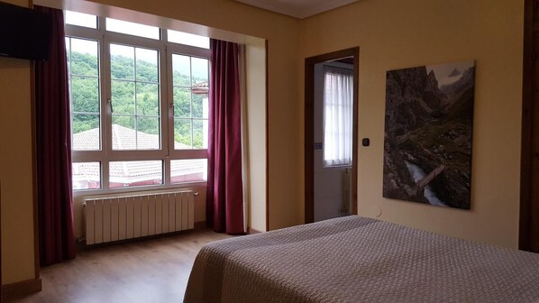 A room with a bed, a window with curtains, a radiator, and a painting on the wall. - Hotel Naranjo De Bulnes (Cabrales)