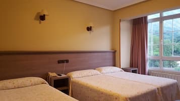 Ett hotellrum med två sängar, ett nattduksbord, en lampa och ett fönster med gardiner.